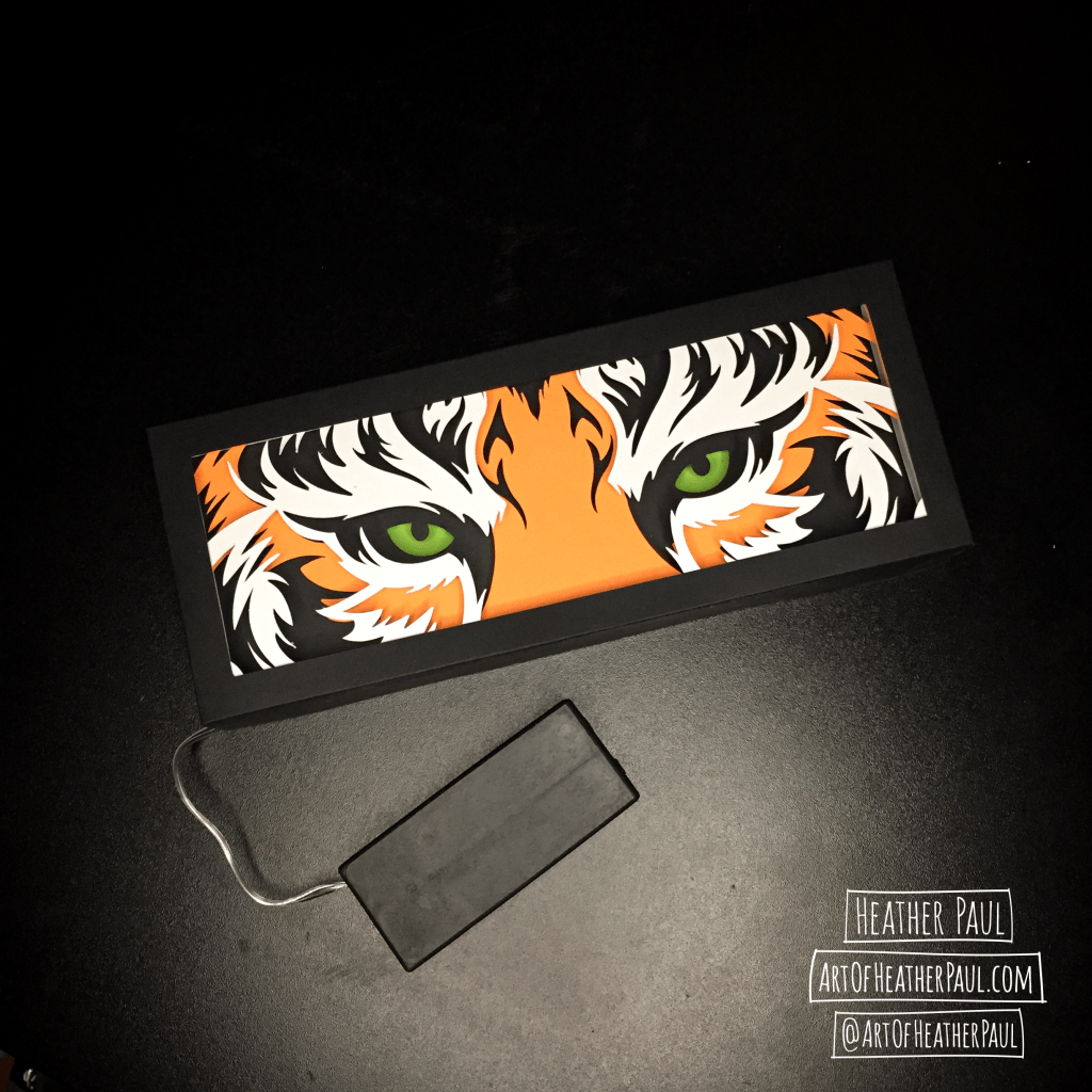 Overhead view of a shadow box made of layers of cut paper making the image of tiger eyes